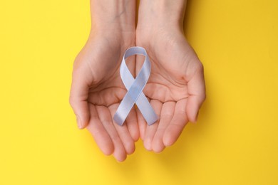 Photo of International Psoriasis Day. Woman with light blue ribbon as symbol of support on yellow background, top view