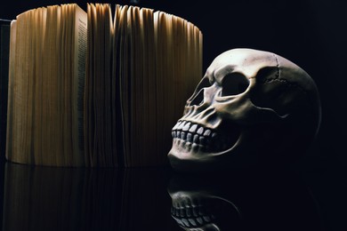 Photo of Human skull and old book on mirror table against black background