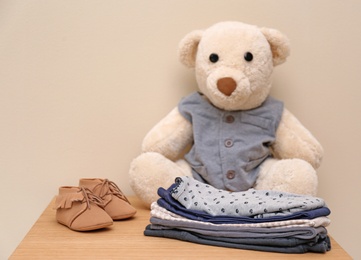 Teddy bear and stylish child clothes on table against light background