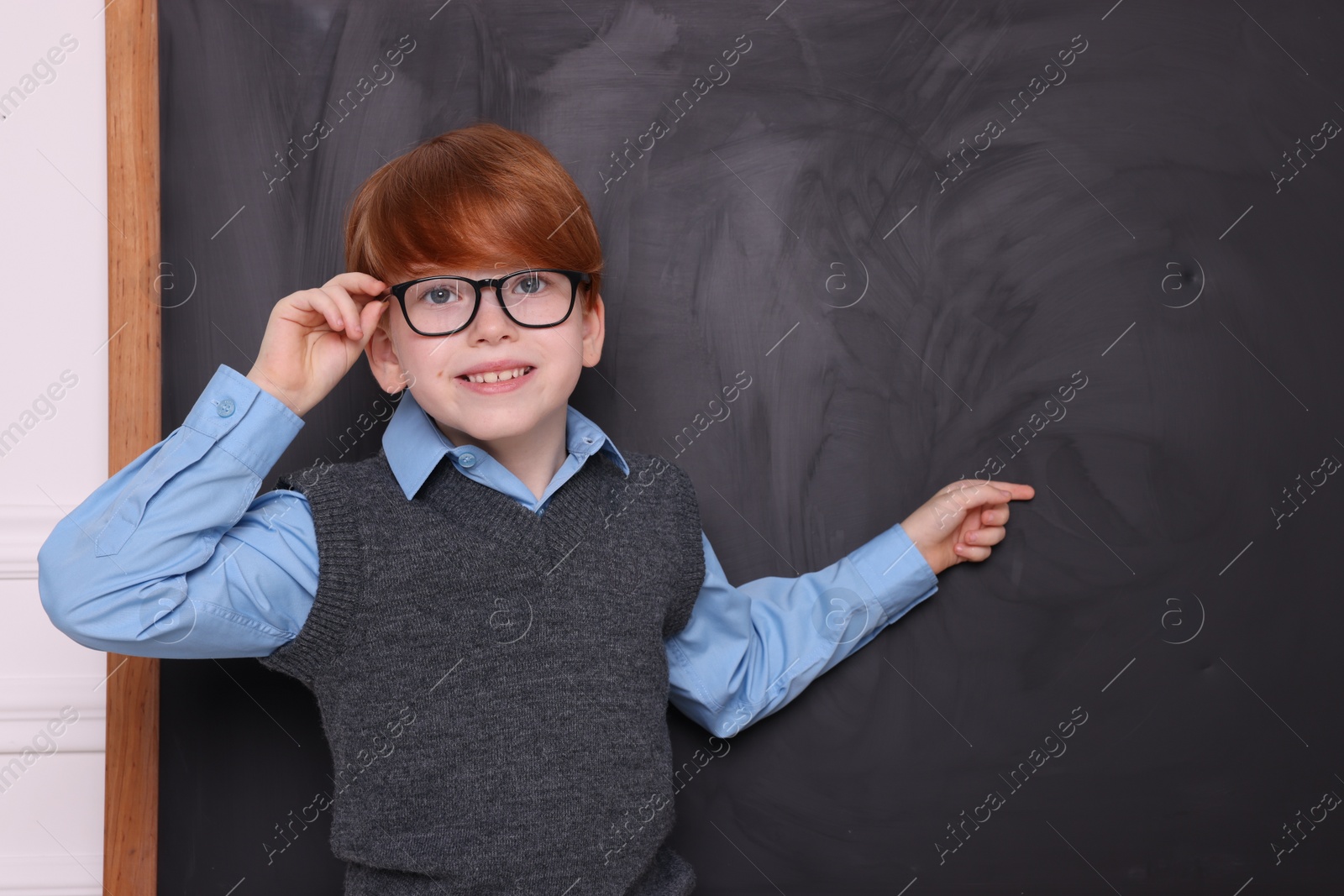 Photo of Smiling schoolboy pointing at something on blackboard