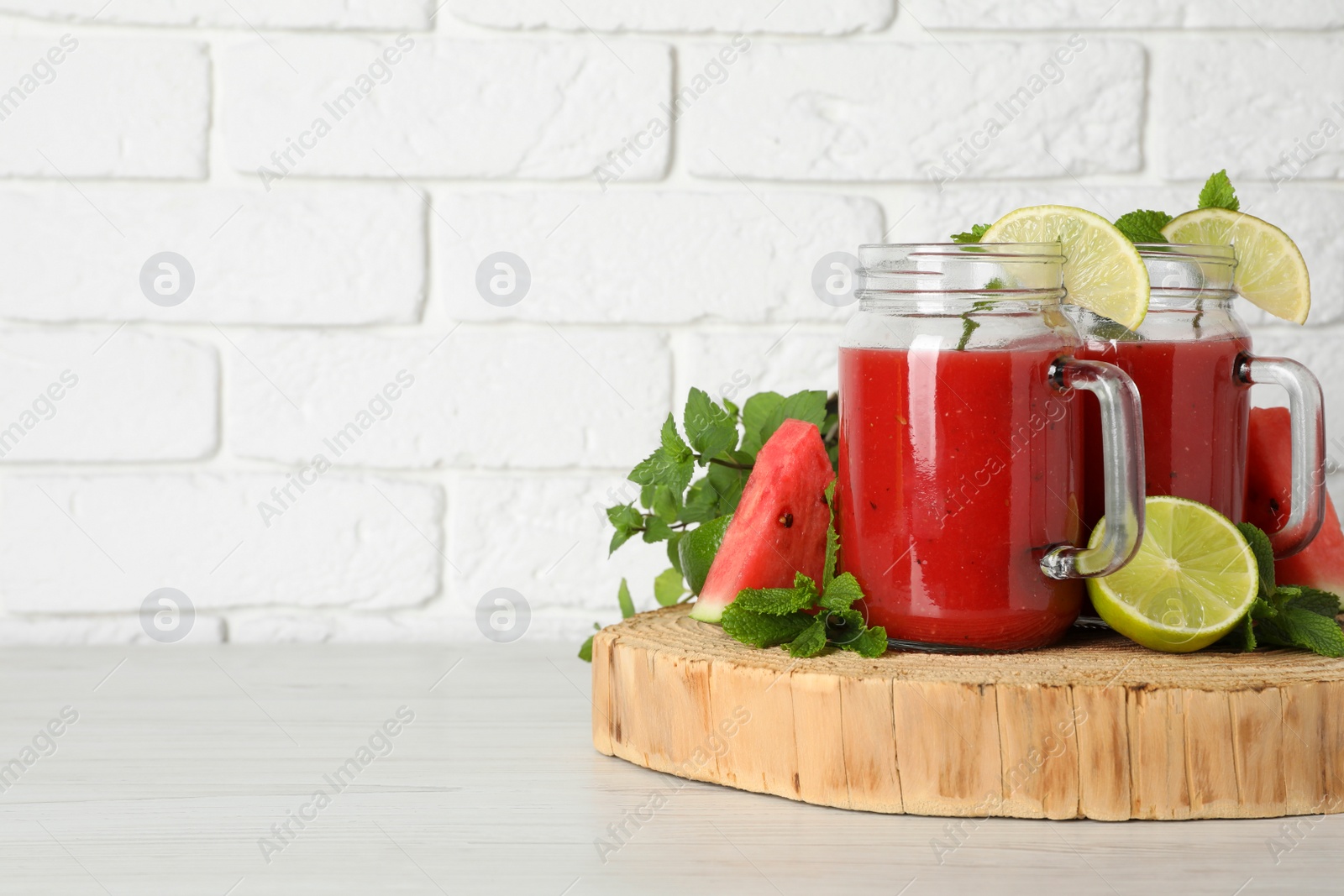 Photo of Tasty summer watermelon drink, limes and mint on white wooden table, space for text