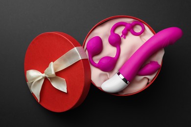 Photo of Pink sex toys in gift box on dark blue background, top view