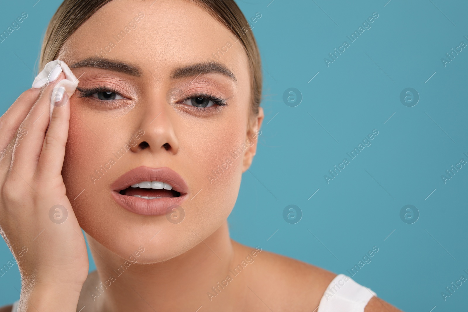 Photo of Beautiful woman removing makeup with cotton pad on light blue background, closeup. Space for text