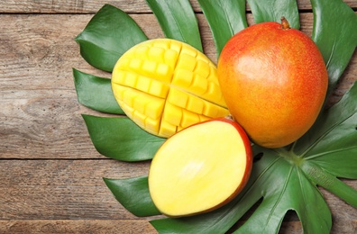 Flat lay composition with ripe mangoes and monstera leaf on wooden background