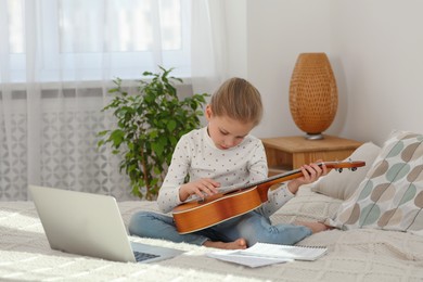 Little girl learning to play ukulele with online music course at home. Time for hobby