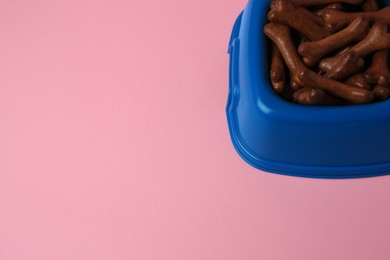 Photo of Blue bowl with bone shaped dog cookies on pink background, space for text