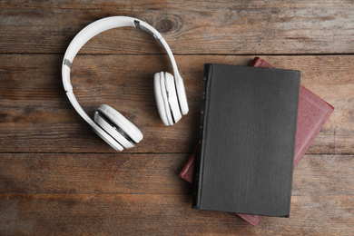 Book and modern headphones on wooden table, flat lay
