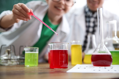 Photo of Teacher with pupil making experiment at table in chemistry class, focus on flask