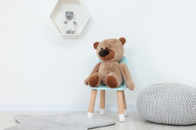 Photo of Teddy bear sitting on chair near white wall in playroom. Stylish kindergarten interior
