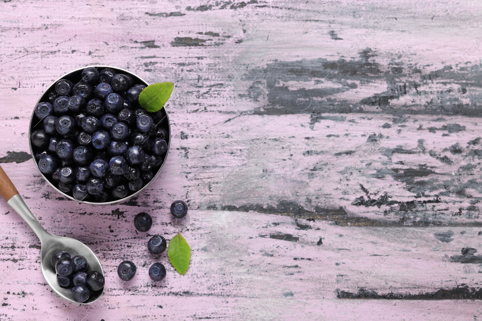 Photo of Ripe bilberries and leaves on wooden rustic table, flat lay. Space for text