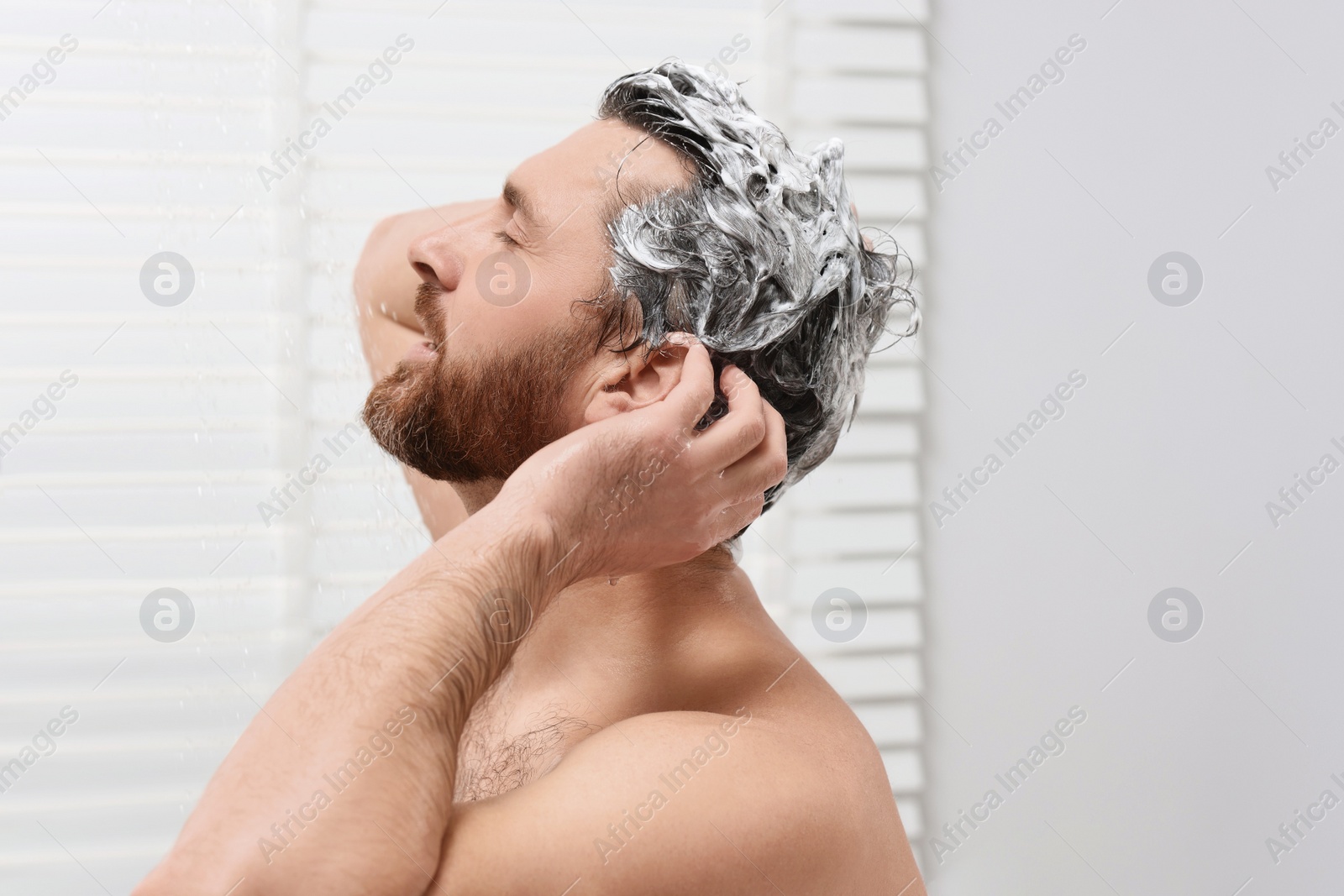Photo of Handsome man washing his hair with shampoo in shower