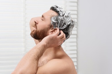 Handsome man washing his hair with shampoo in shower