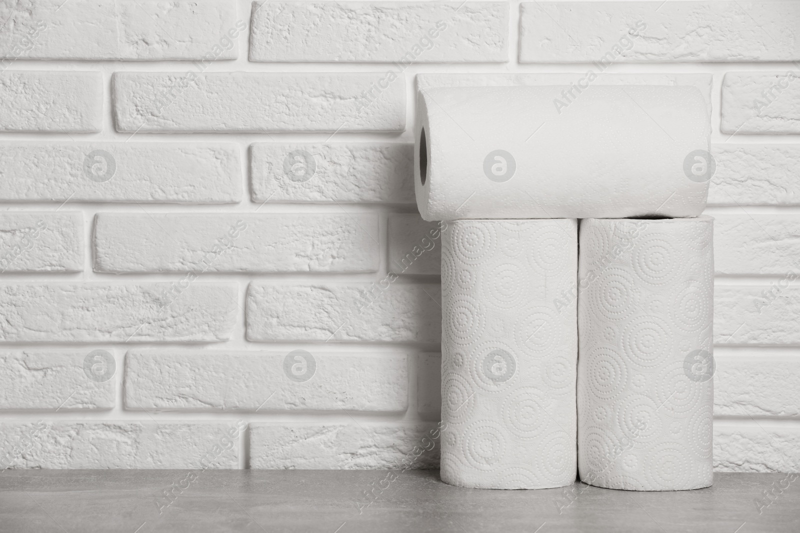 Photo of Rolls of white paper towels on grey table near brick wall. Space for text