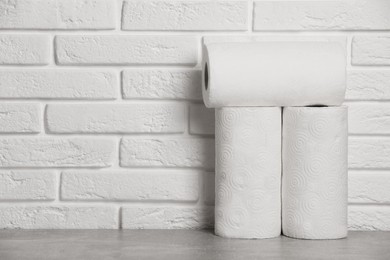 Photo of Rolls of white paper towels on grey table near brick wall. Space for text