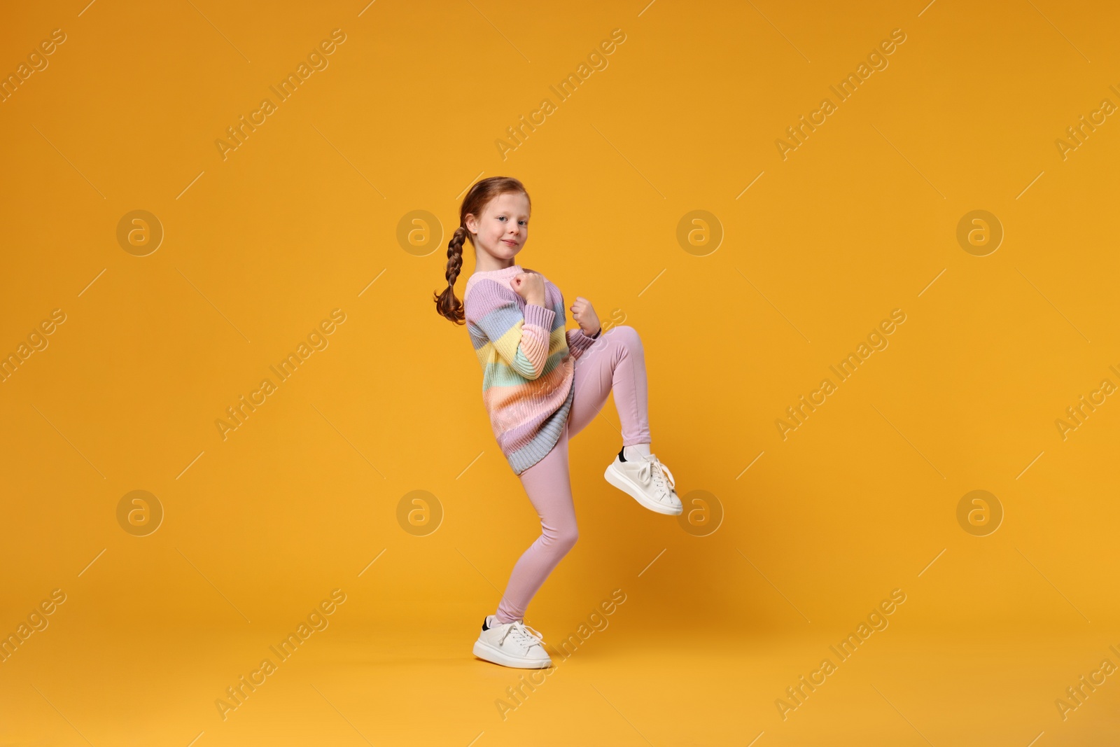 Photo of Cute little girl dancing on orange background