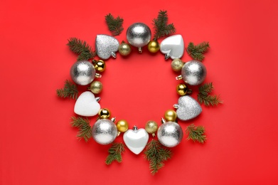 Beautiful festive wreath made of color Christmas balls and fir tree branches on red background, top view