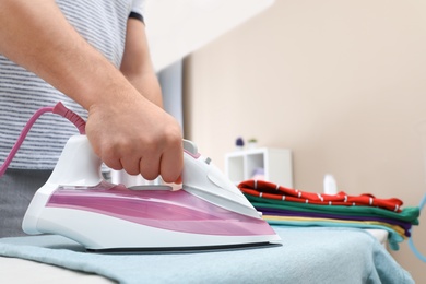 Photo of Man ironing clothes on board at home, closeup. Space for text