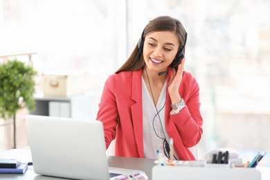 Photo of Young woman talking on phone through headset at workplace