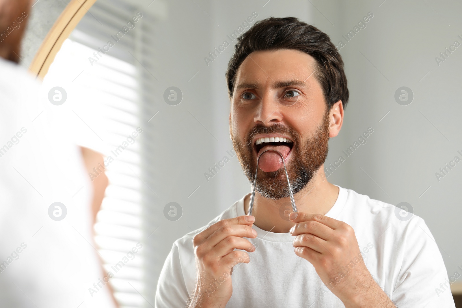 Photo of Handsome man brushing his tongue with cleaner near mirror in bathroom