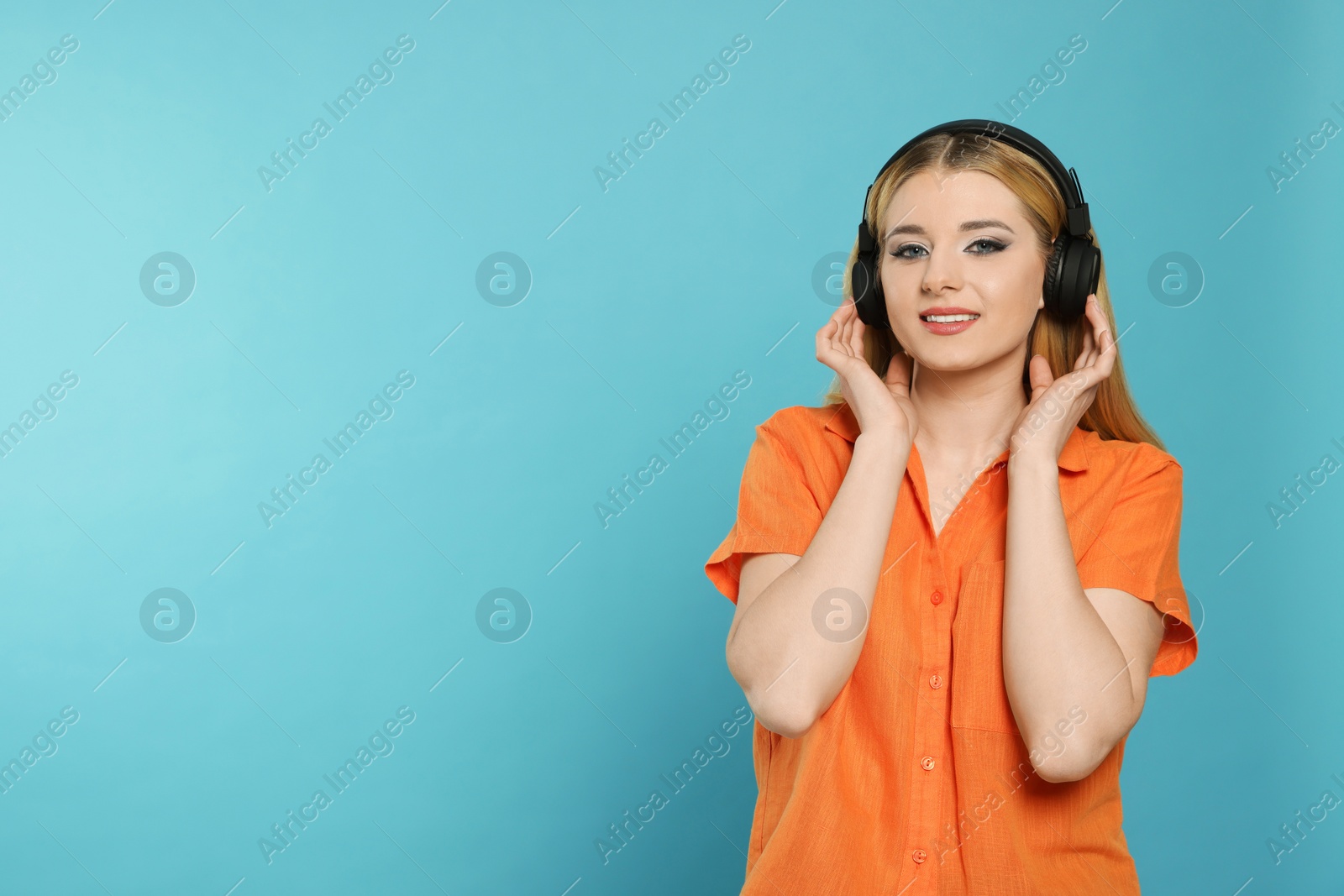 Photo of Portrait of happy woman in headphones enjoying music on light blue background. Space for text