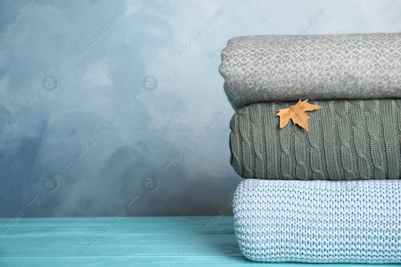 Photo of Stack of soft plaids and dry leaf on light blue wooden table, closeup. Space for text