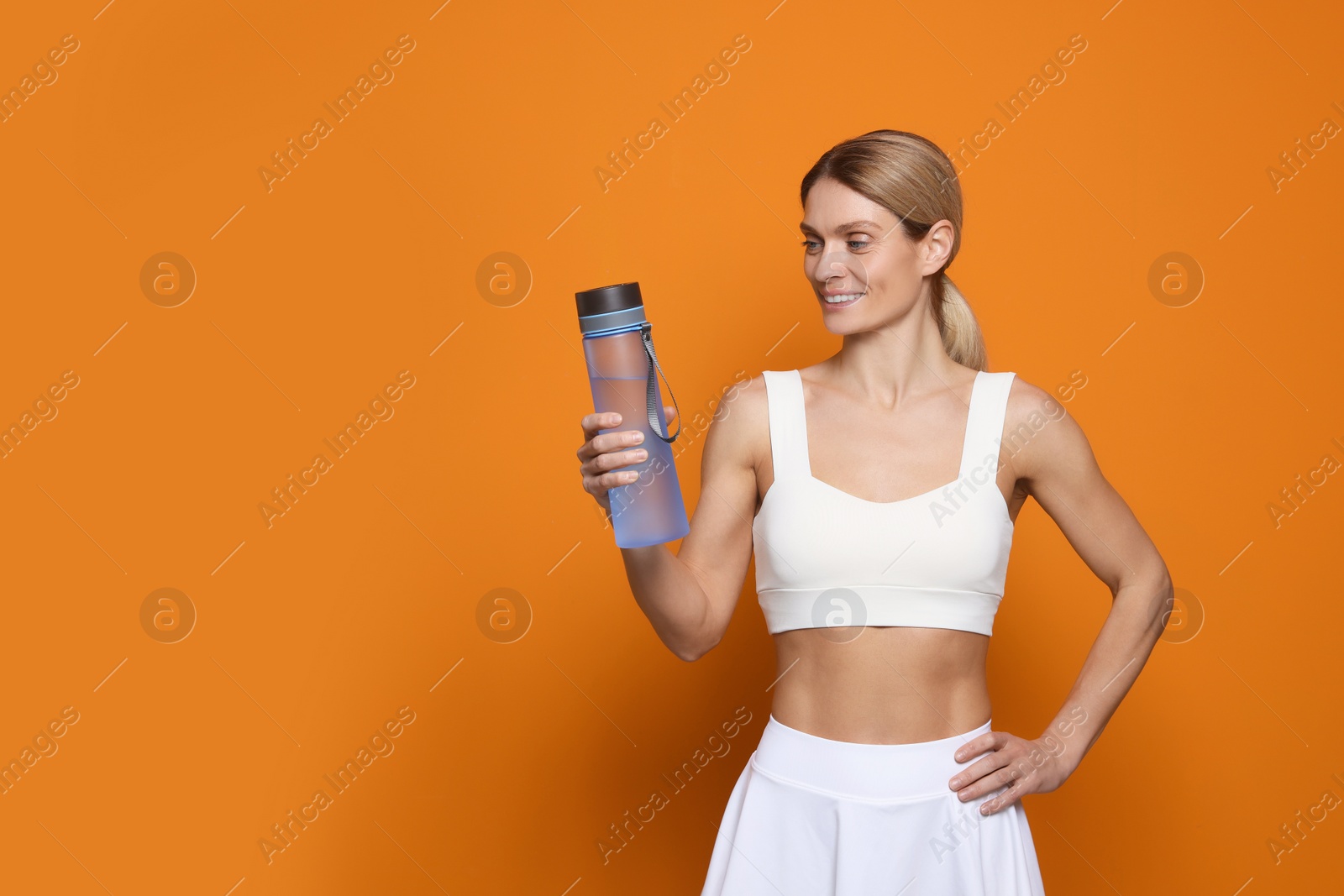 Photo of Sportswoman with bottle of water on orange background, space for text