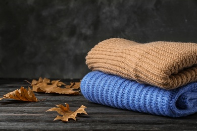 Photo of Stack of folded knitted sweaters and autumn leaves on table. Space for text