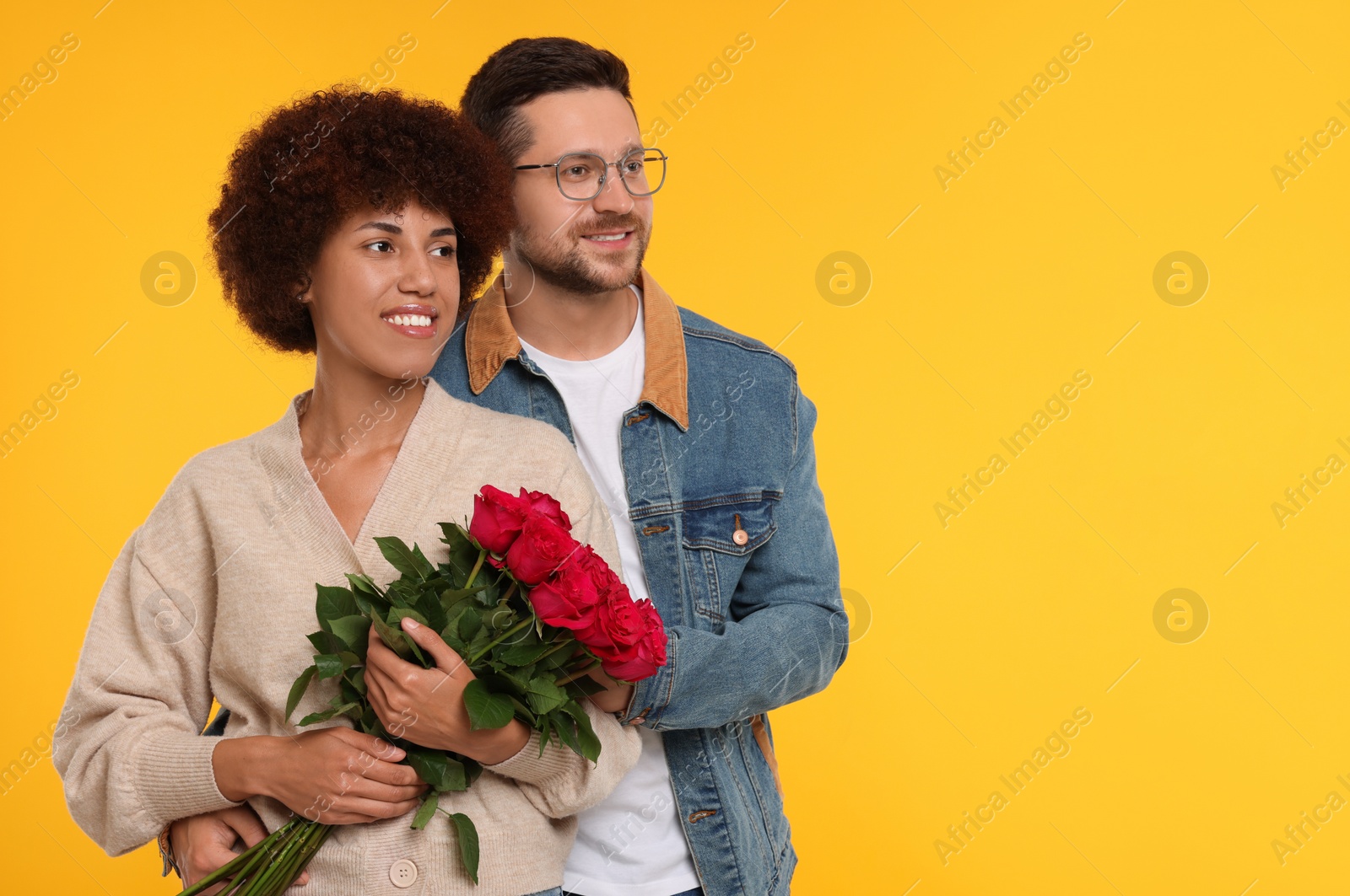 Photo of International dating. Happy couple with bouquet of roses on orange background, space for text