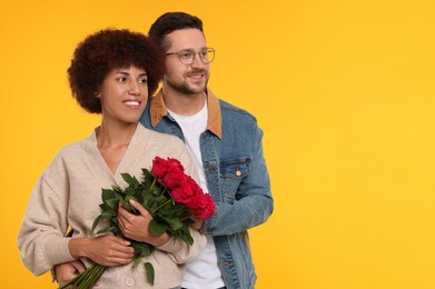 International dating. Happy couple with bouquet of roses on orange background, space for text