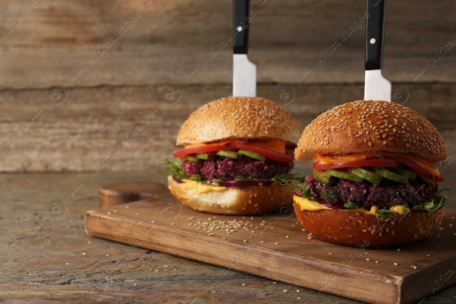 Photo of Tasty vegetarian burgers with beet cutlets, cheese, avocado and tomatoes served on wooden table, selective focus. Space for text