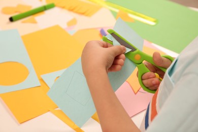 Photo of Little boy cutting color paper with scissors at table indoors, closeup