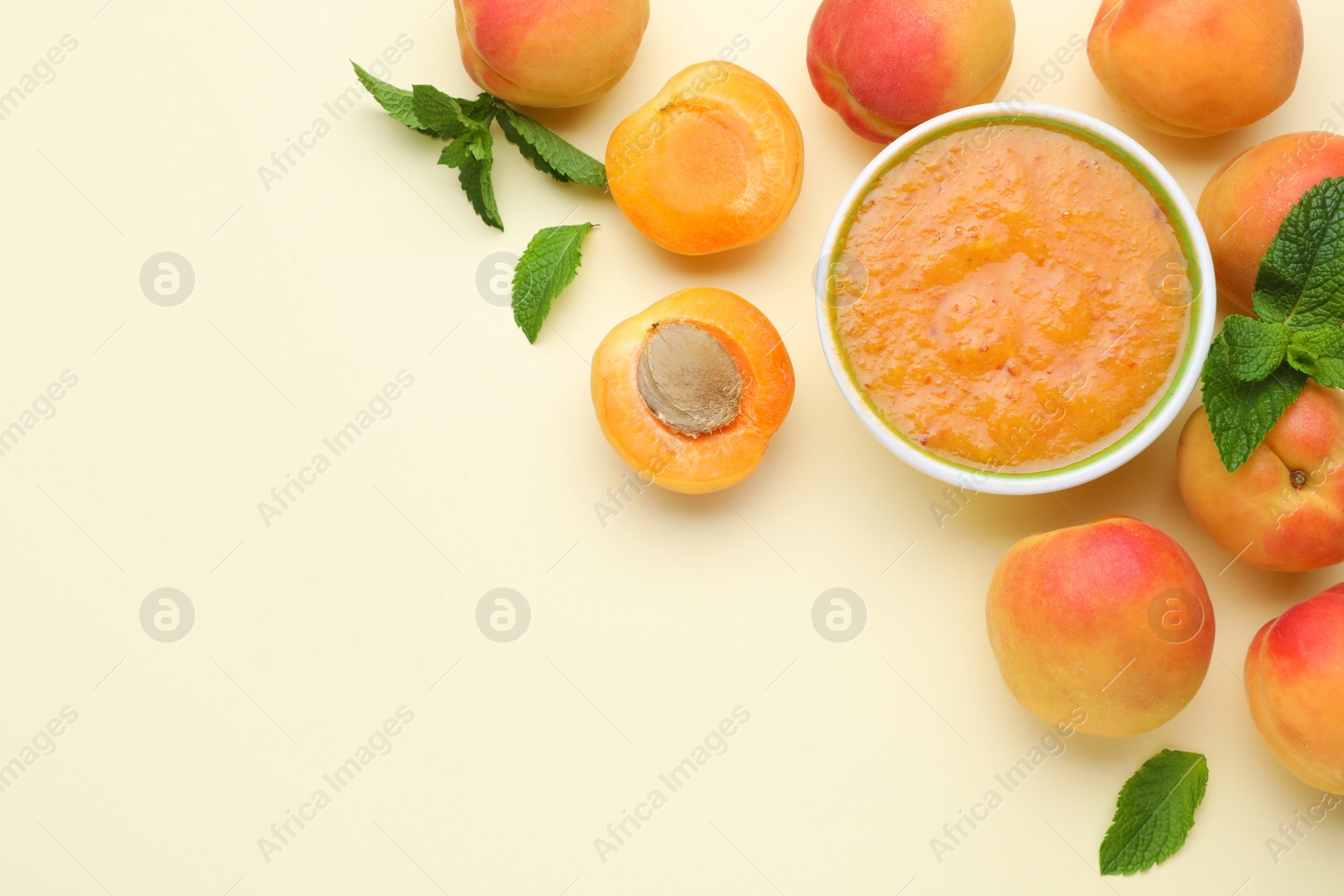 Photo of Apricot puree in bowl and fresh fruits on beige background, flat lay. Space for text