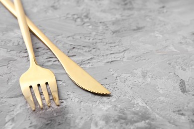 Photo of Stylish cutlery. Golden knife and fork on grey textured table, closeup. Space for text