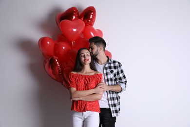 Photo of Happy young couple with heart shaped balloons on light background. Valentine's day celebration