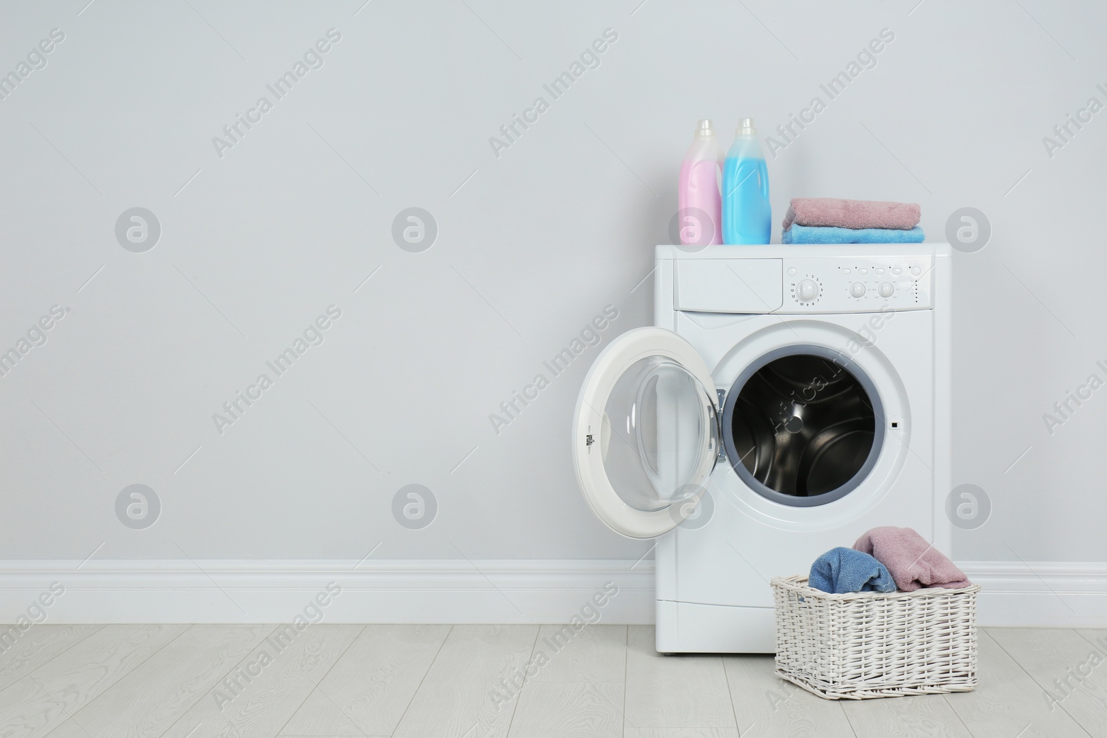 Photo of Modern washing machine with stack of towels, detergents and laundry basket near white wall, space for text
