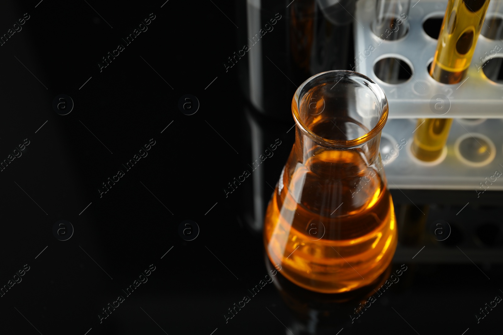 Photo of Laboratory glassware with different types of oil on black background, closeup. Space for text