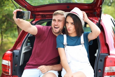 Beautiful young couple taking selfie in car trunk