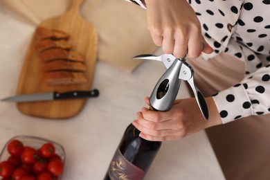 Photo of Romantic dinner. Woman opening wine bottle with corkscrew at table, closeup