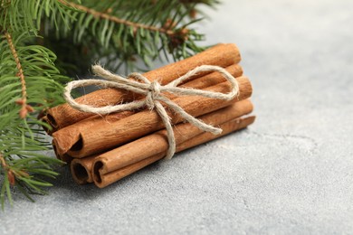 Photo of Bunch of cinnamon sticks and fir branches on grey textured table, closeup. Space for text