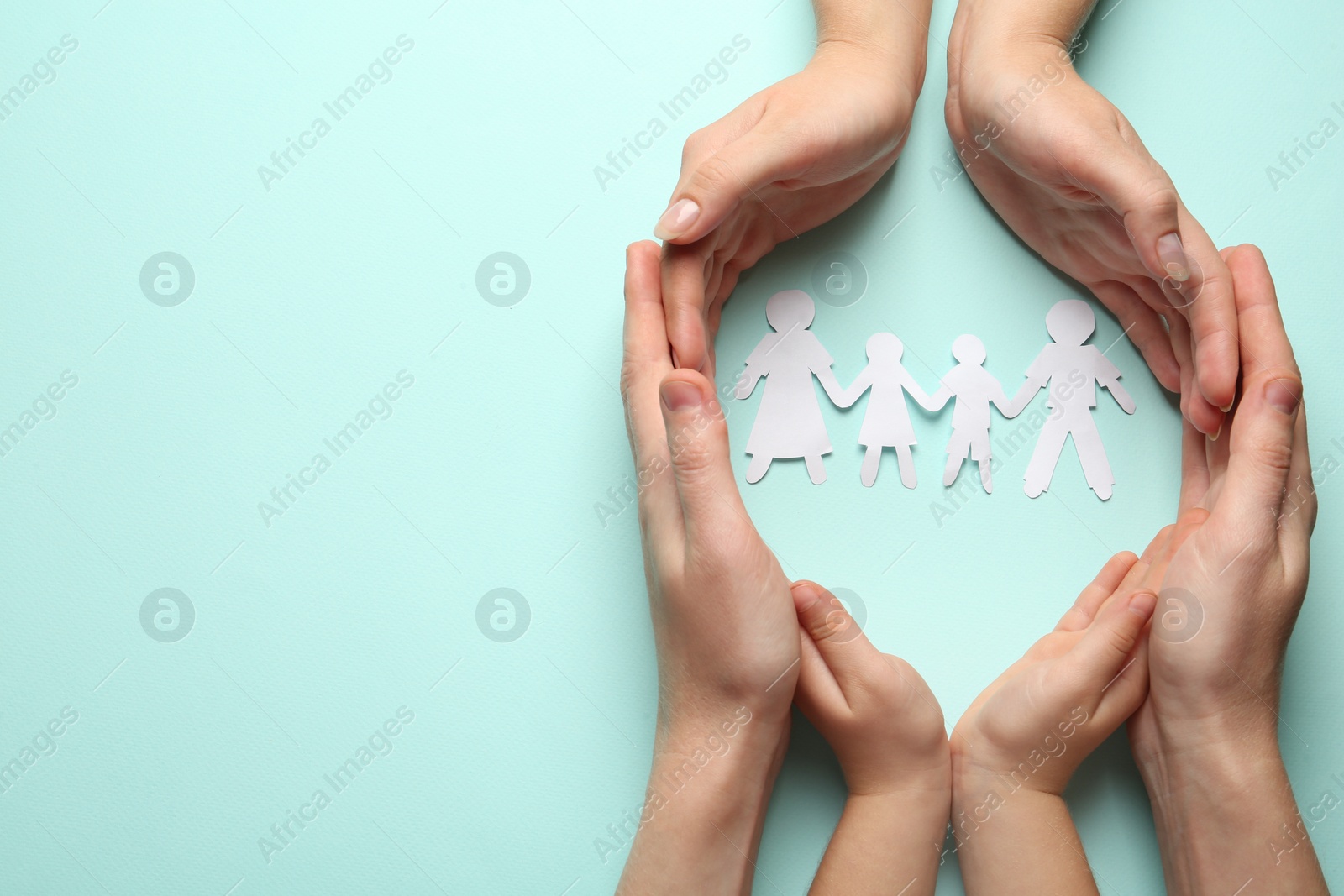 Photo of Parents and child protecting paper cutout of family on light blue background, top view. Space for text