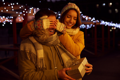 Photo of Woman presenting gift to her boyfriend at Christmas fair. Happy couple