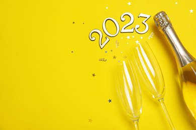 Photo of Happy New Year 2023! Flat lay composition with bottle of sparkling wine on yellow background, space for text