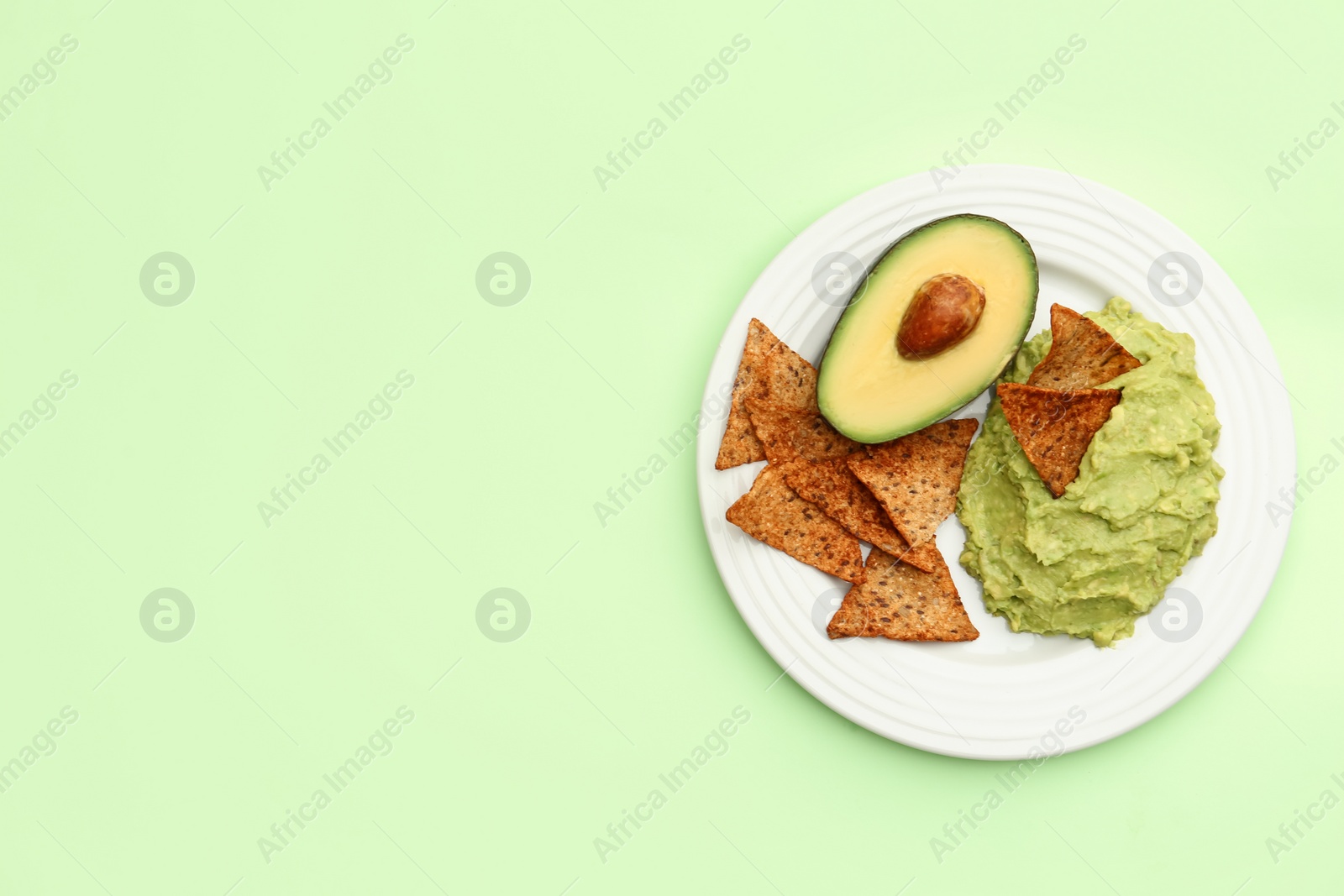 Photo of Delicious guacamole, avocado and nachos on light green background, top view. Space for text