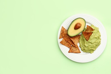 Delicious guacamole, avocado and nachos on light green background, top view. Space for text