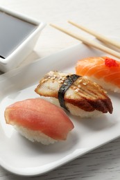 Photo of Plate with delicious nigiri sushi and soy sauce on white wooden table, closeup