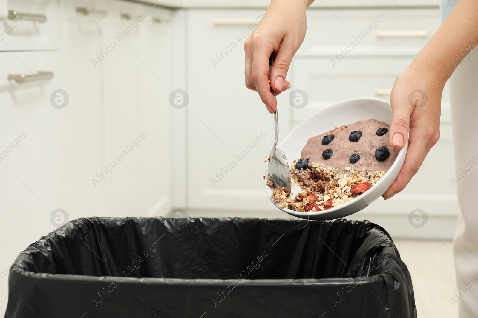 Photo of Woman throwing oatmeal with berries into bin indoors, closeup