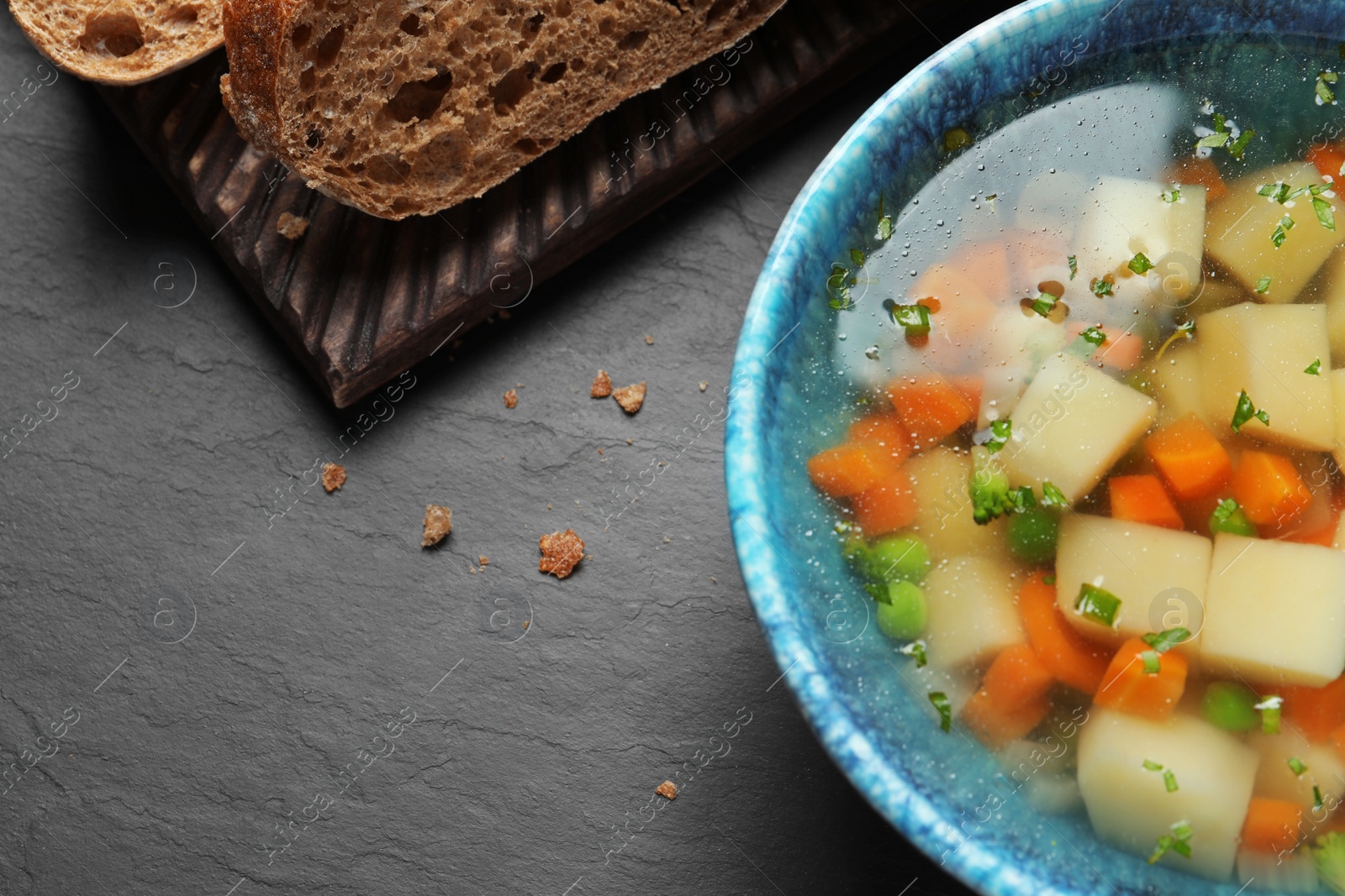 Photo of Bowl of fresh homemade vegetable soup on black background, top view. Space for text