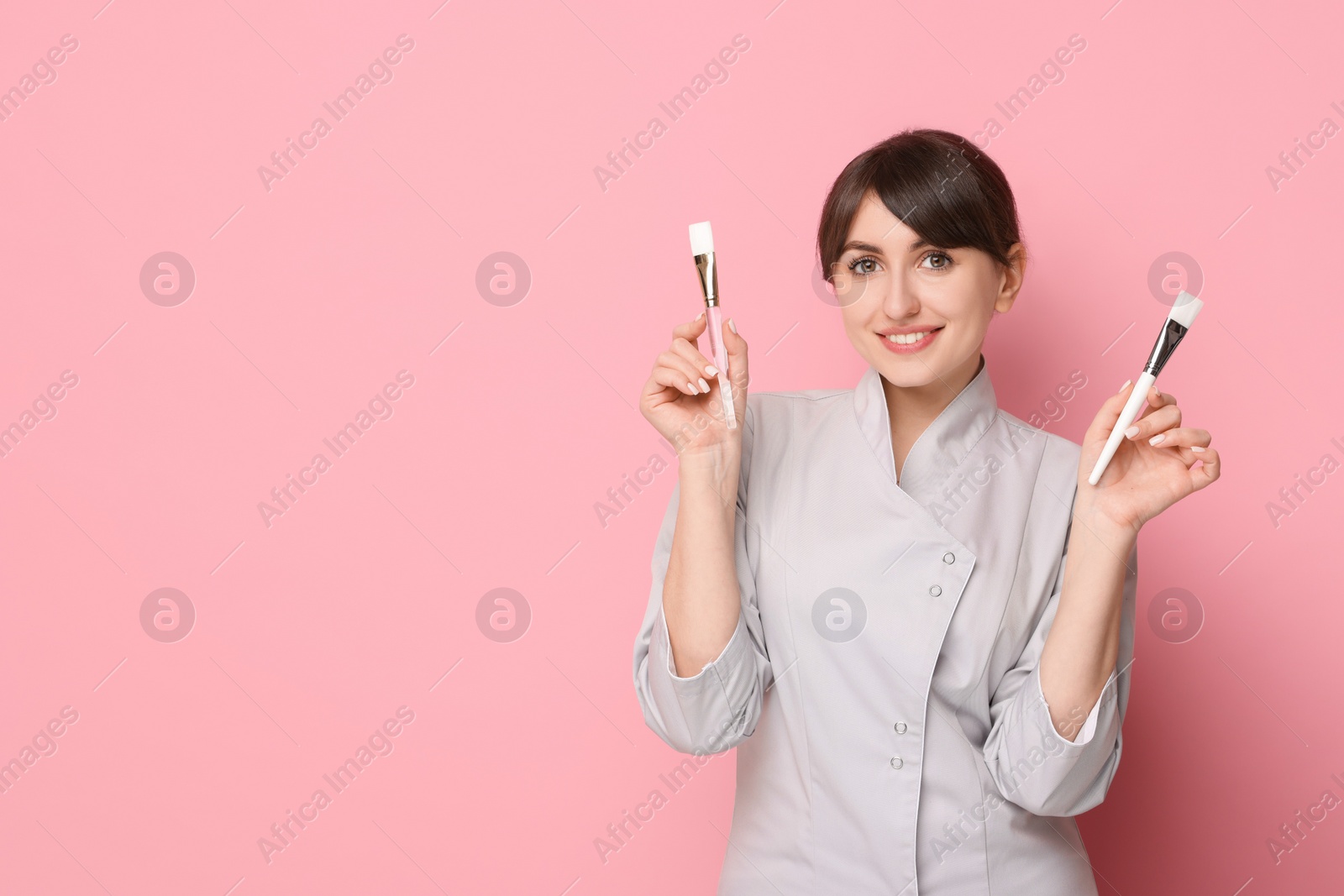 Photo of Cosmetologist with cosmetic brushes on pink background, space for text