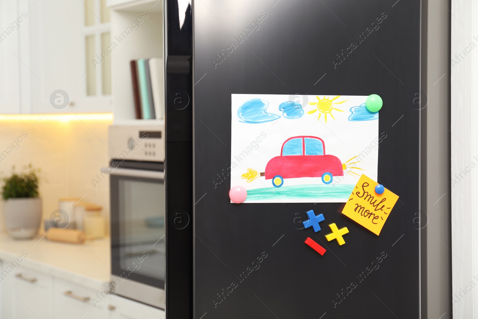 Photo of Modern refrigerator with child's drawing, note and magnets in kitchen