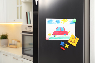 Photo of Modern refrigerator with child's drawing, note and magnets in kitchen